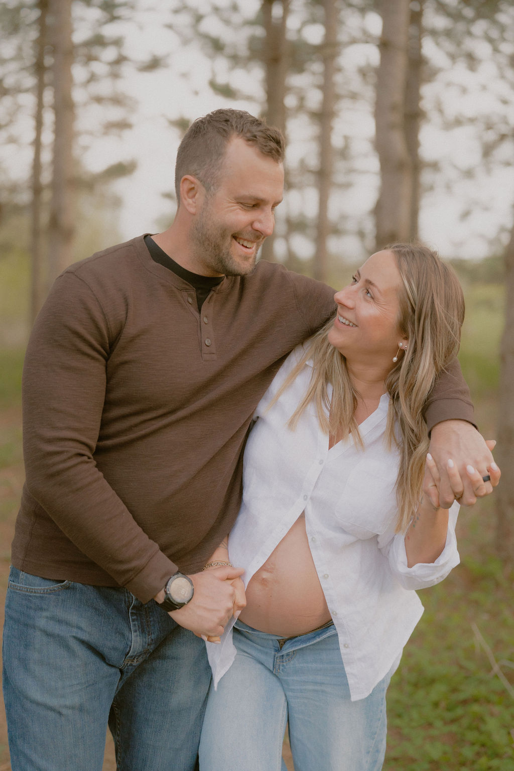 An expectant couple holding hands and walking through a sunlit field during their nostalgic maternity session
